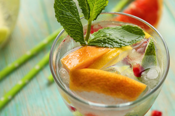 Refreshing cocktail with ice, mint, pomegranate seeds and slices of fruits on blue wooden background