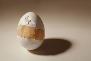 Cracked egg with plaster on color background