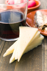 sheep cheese in portions and glass of wine on wood