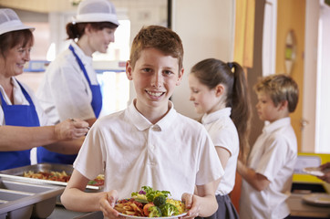 Caucasian schoolboy holds plate of food in school cafeteria