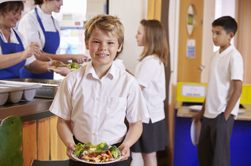 Fototapeta na wymiar Blonde haired boy holding plate of food in school cafeteria