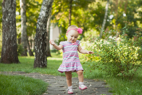 Baby girl walking outdoors dressed in pink stripped dress. Happy kid. Happy childhood.