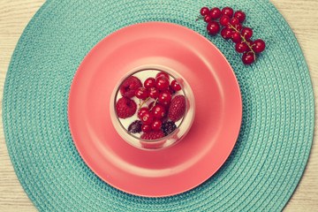 Frutos rojos frescos y naturales dentro de un vaso sobre un plato rosa. Vista superior