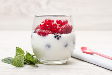 Vaso de yogur con frutos rojos sobre una mesa rústica de madera. Vista de cerca y de frente