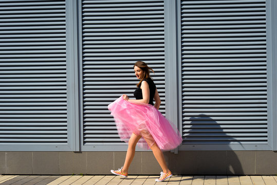 Beautiful sexy young hipster girl outdoors.Posh woman with long brunette  hair evening makeup wearing light fluffy pink rosy skirt and vans sneakers  posing outdoors in the city urban style in summer Stock