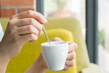 Hand of young woman stirring spoon in cup of coffee expresso
