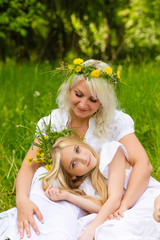Beautiful and happy mum and daughter with wreaths on the head outdoors in the summer