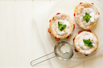 Preparing homemade choux pastry rings with cottage cheese cream and strawberries decorated mint leaves on white wooden background