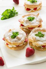 Homemade choux pastry rings with cottage cheese cream and strawberries decorated mint leaves on white wooden background