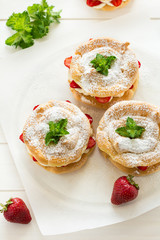 Homemade choux pastry rings with cottage cheese cream and strawberries decorated mint leaves on white wooden background