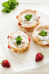 Homemade choux pastry rings with cottage cheese cream and strawberries decorated mint leaves on white wooden background