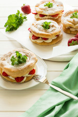 Homemade choux pastry rings with cottage cheese cream and strawberries decorated mint leaves on white wooden background