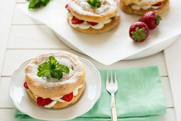 Homemade choux pastry rings with cottage cheese cream and strawberries decorated mint leaves on white wooden background
