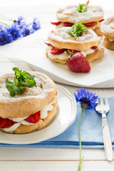 Homemade choux pastry rings with cottage cheese cream and strawberries decorated mint leaves on white wooden background