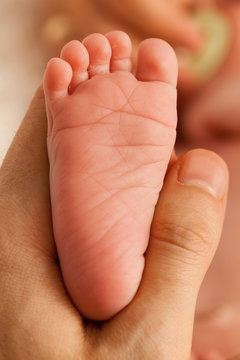 Father holding the foot of his newborn kid. Close up