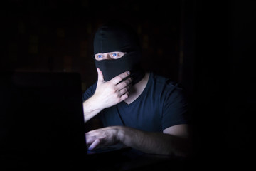 Hacker in black mask with laptop
