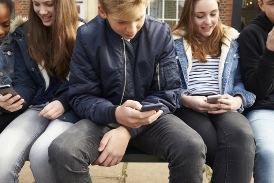 Teenage Friends Using Mobile Phones In Urban Setting