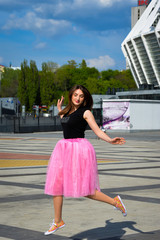 Beautiful sexy young hipster girl outdoors.Posh woman with long brunette hair evening makeup wearing light fluffy pink rosy skirt and vans sneakers posing outdoors in the city urban style in summer