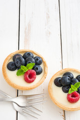Delicious tartlets with raspberries and blueberries
on white wood