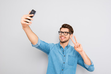 Happy man in glasses making selfie on smartphone and showing two