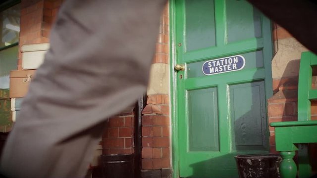 People pass a Station Master's door on an old British Railway station's platform