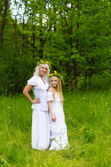 Beautiful and happy mum and daughter with wreaths on the head outdoors in the summer