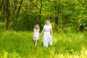 Naklejka na ściany i meble Beautiful family goes hand in hand. Happy family resting on the nature in the summer. Mom and daughter with wreath in the flowers in the park