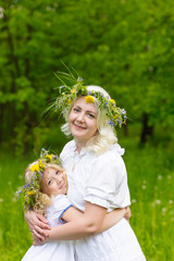 Beautiful and happy mum and daughter with wreaths on the head outdoors in the summer