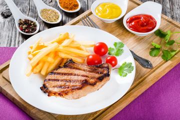 grilled pork chops on a white dish with french fries