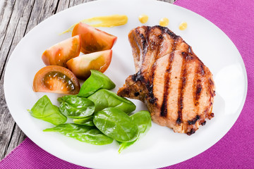 grilled pork chops with slices of black tomatoe and spinach leav