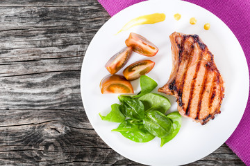 grilled pork chops on with slices of black tomatoes, spinach