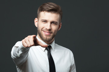 Young handsome businessman pointing at you  isolated on gray bac