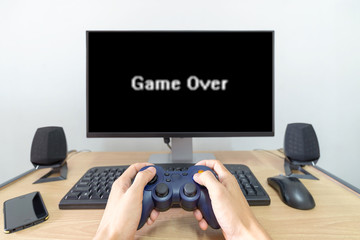 Hands man hold gamepad  in front of tv screen with game over word