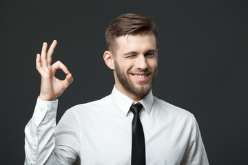 Handsome businessman showing okay sign on dark gray background.