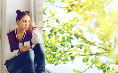 teenage girl sitting on windowsill with smartphone