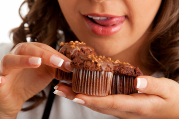 Young woman eating chocolate muffin, close up, horizontal shot, tongue sticking out