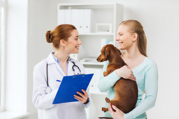 happy woman with dog and doctor at vet clinic