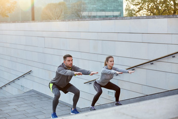 couple doing squats on city street stairs