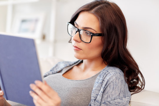 young woman in glasses reading book at home