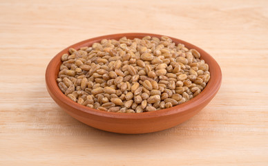 Small bowl of red winter wheat berries on wood table