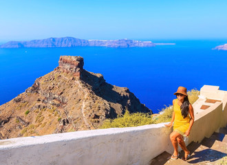 Attractive woman wearing hat and yellow dress enjoying the view of volcanic island,walking up stairs on Santorini, Mediterranean sea, Greece