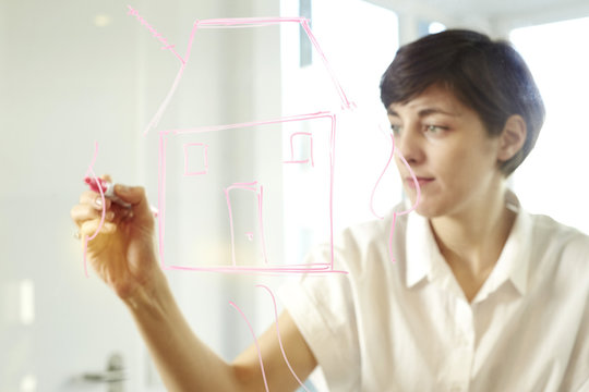 Woman drawing a house on glass pane in an office
