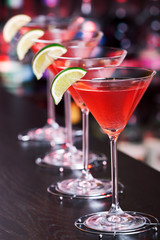 Row of Cosmopolitan cocktails shot on a bar counter in a nightclub. Vertical shot