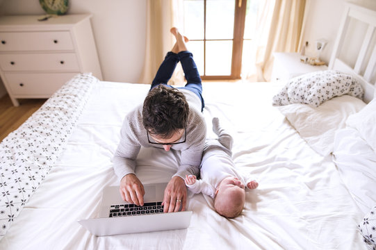 Father with baby lying on bed using laptop