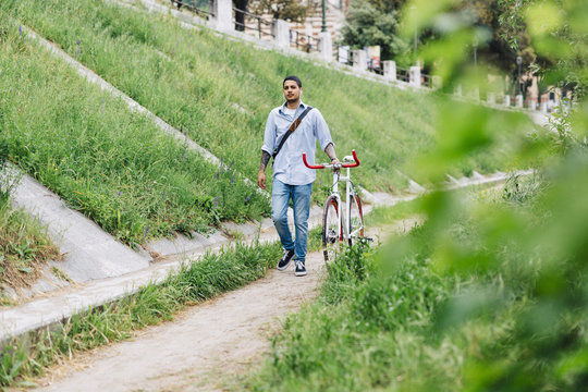 Young man walking with a bicycle on a path