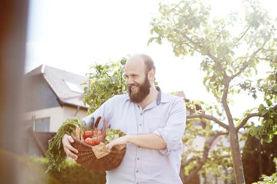 Young man standing in garden, basket with fresh vegetables