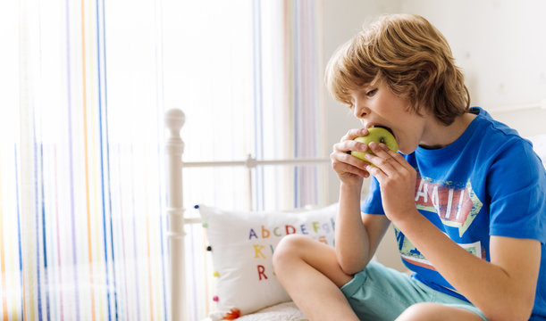 Portrait of boy sitting on the couch eating an apple