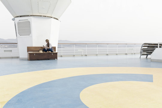 Woman sitting on deck of cruise liner looking at her smartphone