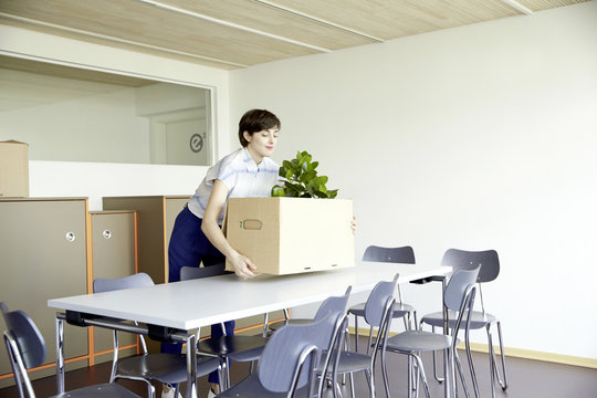 Smiling woman carrying cardboard box in new office