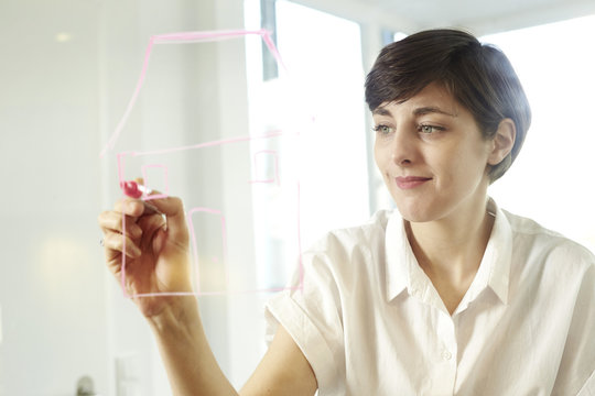 Portrait of woman drawing a house on glass pane in an office